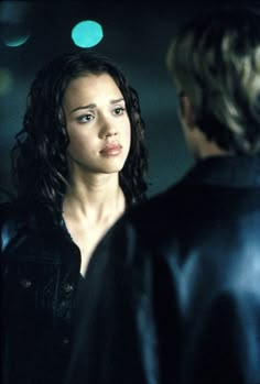 a woman standing next to a man in a black leather jacket looking at each other