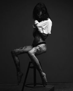 a woman sitting on top of a stool with her legs crossed and tattoos all over her body