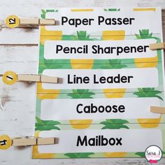 four pineapple name tags with clothes pins attached to them on a white wooden background