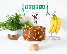 a birthday cake with a monkey on top and bananas in the back ground next to it