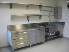 an industrial kitchen with stainless steel cabinets and sink in the center, under shelving