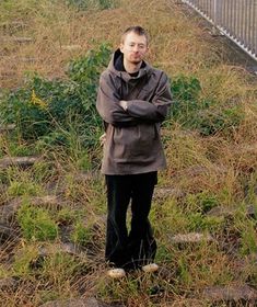 a man is standing in the grass with his arms crossed and looking at the camera