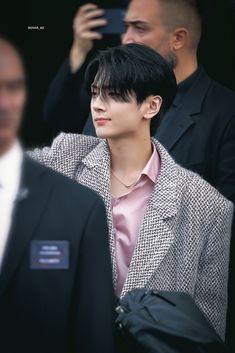 a man with black hair wearing a suit and pink shirt standing next to other men