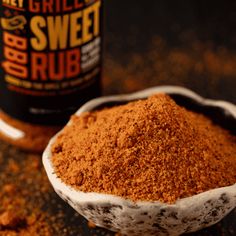 a bowl filled with ground spices next to a bottle of sweet rubs on a table