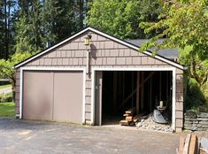 a garage with the door open in front of trees and rocks on the ground next to it