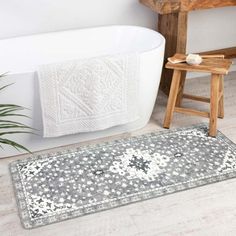 a bath tub sitting next to a wooden stool in a bathroom with a rug on the floor