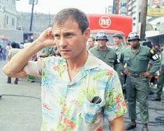 a man in a hawaiian shirt is standing on the street with other uniformed men behind him