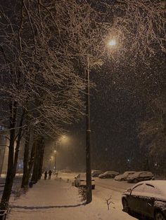 a snowy street with cars parked on it and people walking in the snow at night