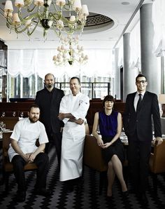 a group of people standing in front of a chandelier and dining room table