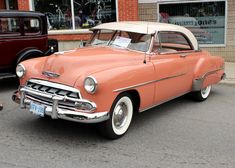 an orange and white car parked in front of a building next to another red car