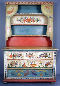 an old dresser with painted drawers and curtains on the top, sitting against a blue wall