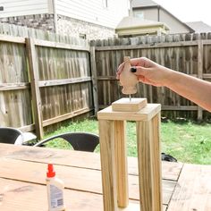 a person holding a piece of wood on top of a wooden table next to a bottle