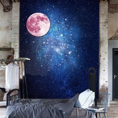 a room with a bed, chair and wall mural that has the moon on it