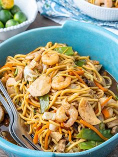 a blue bowl filled with noodles, shrimp and veggies on top of a wooden table