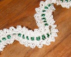 a piece of white and green crochet with beads on it sitting on top of a wooden table