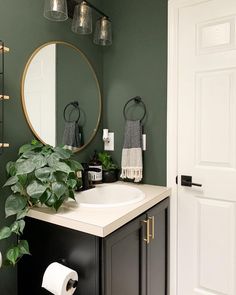 a bathroom with green walls and a round mirror on the wall above the sink is a plant