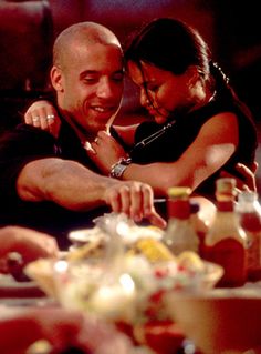 a man and woman are hugging at a table with food on the plate in front of them