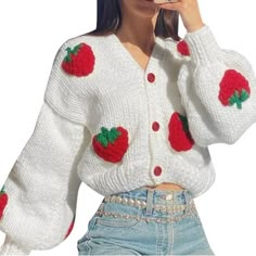 a woman sitting on top of a bed wearing a white sweater with red strawberrys