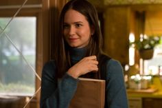 a woman holding a brown shopping bag in her right hand and looking at the camera