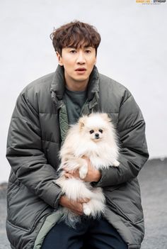 a man holding a small white dog in his lap while wearing a puffy coat