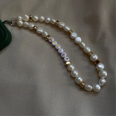 a white pearl beaded necklace on a bed with a green purse in the background