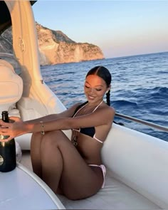 a woman sitting on the back of a boat with a bottle of wine in her hand