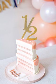 a pink and white cake with the number twenty five on it's top is sitting in front of balloons