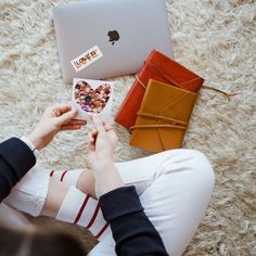 a woman is sitting on the floor with her laptop and various items in front of her