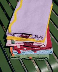 four folded towels sitting on top of a green park bench next to each other in different colors