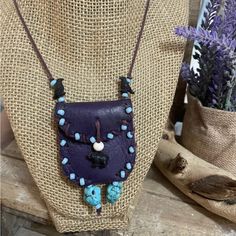 a purple and blue necklace on a mannequin with lavender flowers in the background