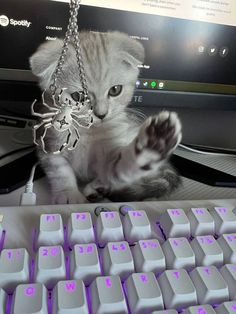 a kitten is playing with a key chain on a computer keyboard and it's paw