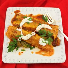 a white plate topped with enchiladas covered in sauce and garnish