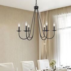 a chandelier hanging over a dining room table with white chairs and place settings