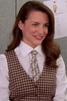 a woman wearing a dress shirt and tie in an office cubicle smiling at the camera