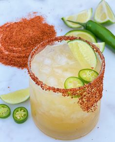 a drink with limes and spices on the rim next to sliced jalapenos