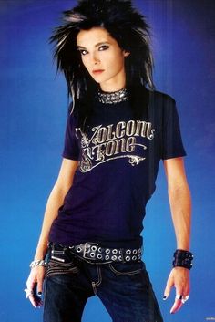 a woman with black hair and piercings standing in front of a blue background