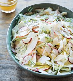 a salad with radishes and apples in a bowl next to a glass of beer