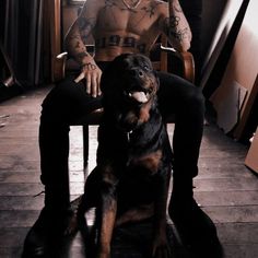 a man with tattoos sitting in a chair next to a black and brown dog on the floor