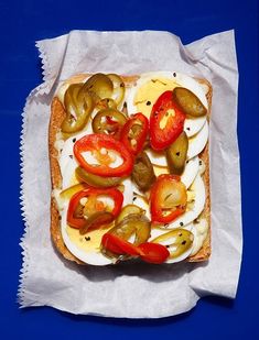 an open faced sandwich with pickles, tomatoes and cheese on it sitting on a piece of wax paper