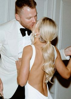 a man in a tuxedo kissing a woman's back with her hand on her hip