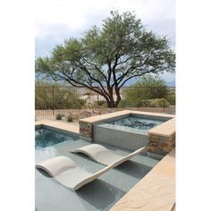 an outdoor swimming pool with chaise lounges next to it and a tree in the background