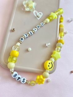 a cell phone case with beads and smiley face charms on the front, sitting on a pink surface