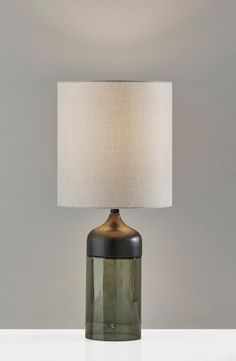 a green glass table lamp with a white linen shade on the base and a grey wall behind it