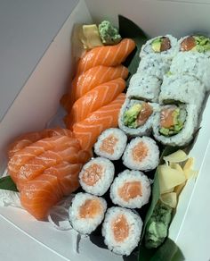 sushi and sashimi in a white box with green leaves