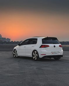 a white car parked in an empty parking lot with the sun setting behind it,