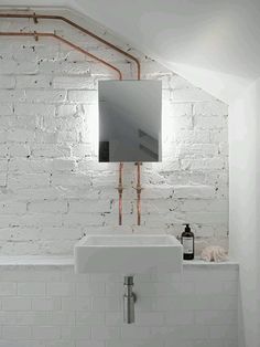 a white bathroom with exposed pipes and a mirror on the wall over the sink,