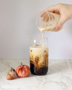 someone is pouring something into a glass on the counter next to some pumpkins and an onion