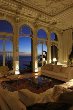 a living room filled with lots of furniture and large windows overlooking the ocean at night