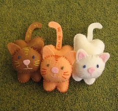 three stuffed animals sitting on top of a green carpet next to an orange and white cat