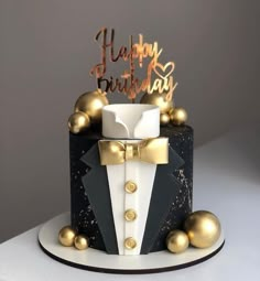 a black and white cake with gold decorations on it's side, topped with a tuxedo